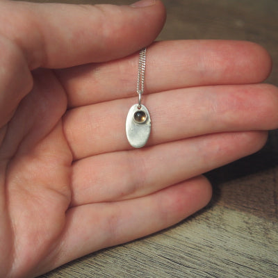 Collier pendenti en argent avec pendentif oval en quartz fumé porté dans une main.